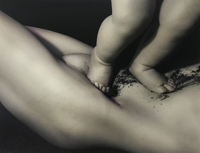 A black and white photograph of a baby standing on a woman's tummy.