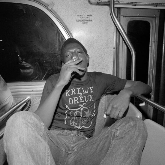 A black and white photograph of a young boy smoking on a bus.