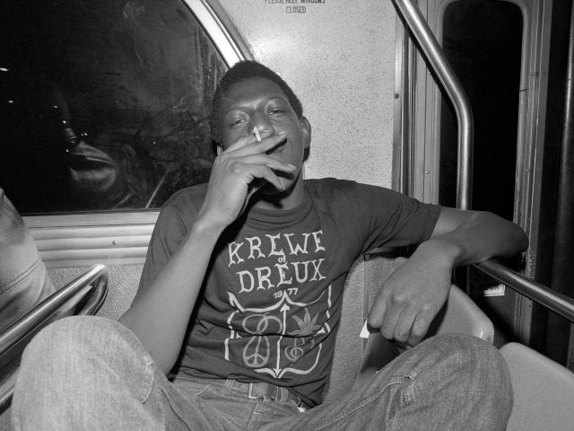 A black and white photograph of a young boy smoking on a bus.