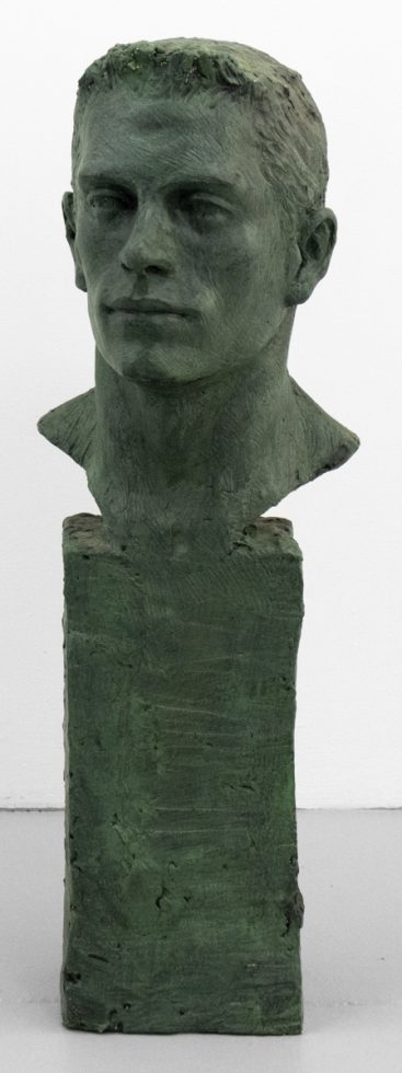 A green bust of a man's face in an oxidized green.
