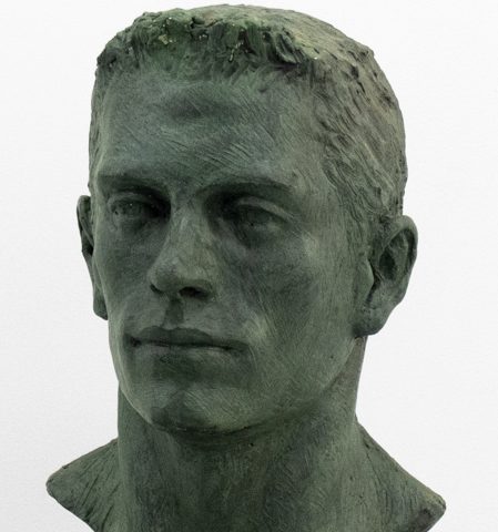 A green bust of a man's face in an oxidized green.