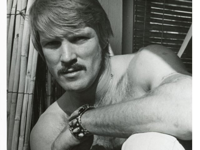 A black and white portrait of a handsome shirtless man.