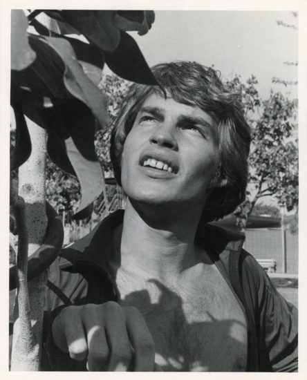 A black and white photograph of a young man with leaves.