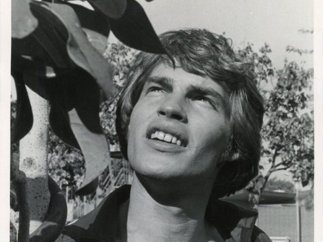 A black and white photograph of a young man with leaves.
