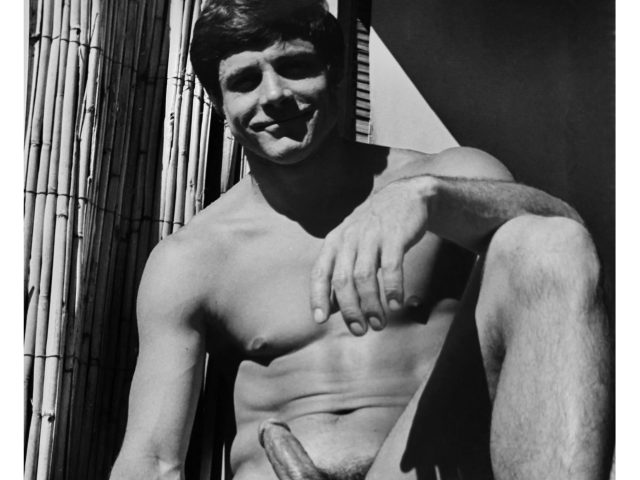 A black and white photograph of a nude man sitting in the sun.