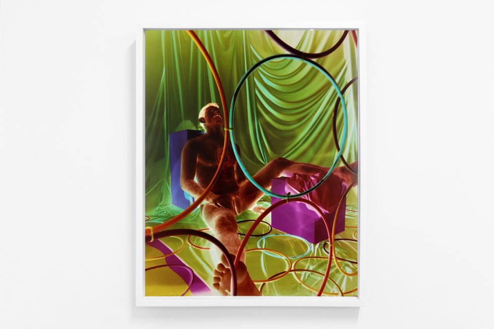 A photograph of a white-walled gallery space with colorful photographs on display.