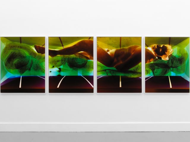 A photograph of a white-walled gallery space with colorful photographs on display.