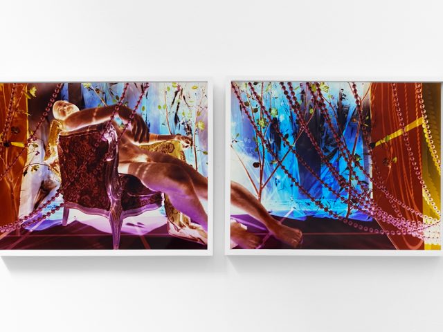 A photograph of a white-walled gallery space with colorful photographs on display.