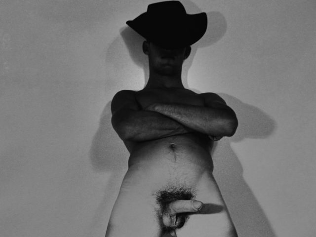 A black and white nude photograph of a man in a cowboy hat.