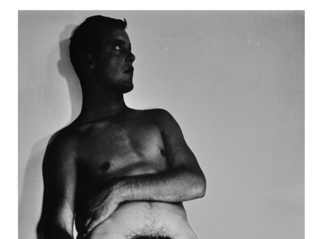 A black and white nude photograph of a man in a cowboy hat.