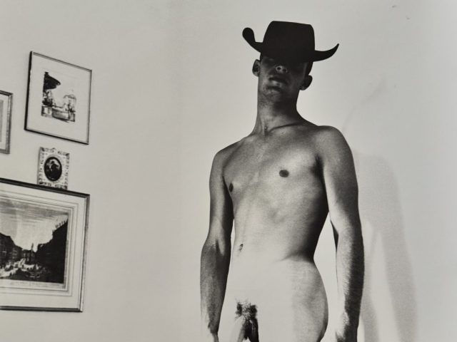 A black and white nude photograph of a man in a cowboy hat.