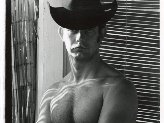 A black and white photograph of a shirtless man in a black cowboy hat.
