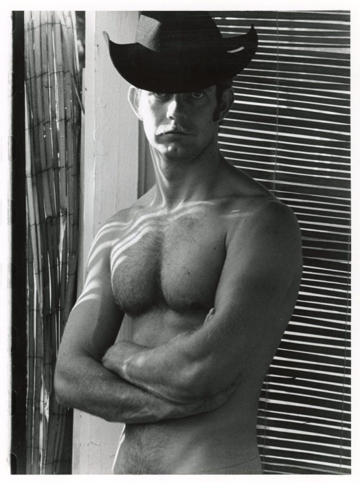 A black and white photograph of a shirtless man in a black cowboy hat.