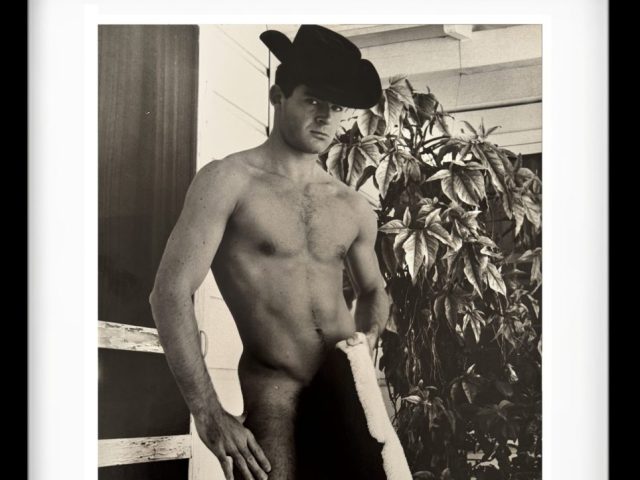 A black and white photograph of a shirtless man holding a jacket.