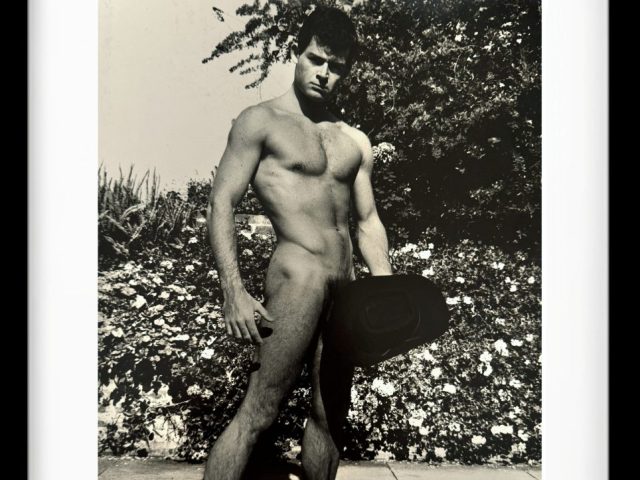 A black and white photograph of a nude man standing outside.