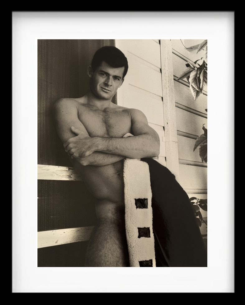 A black-and-white photograph of a handsome man in the nude with a jacket covering his intimate region.