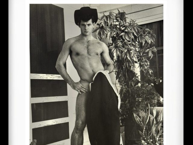A black and white photograph of a handsome shirtless man standing.
