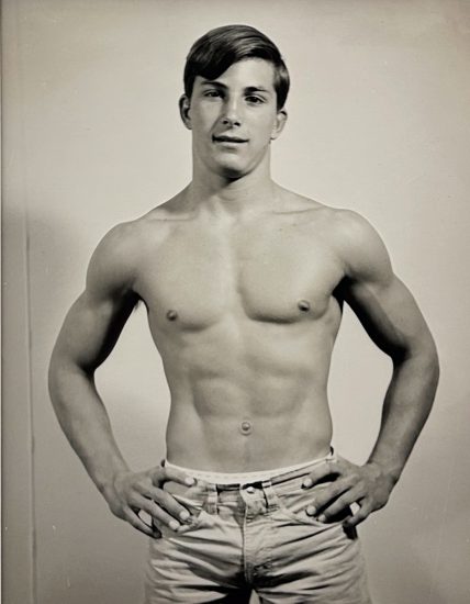 A black and white photograph of a shirtless man with his hands on his hips.