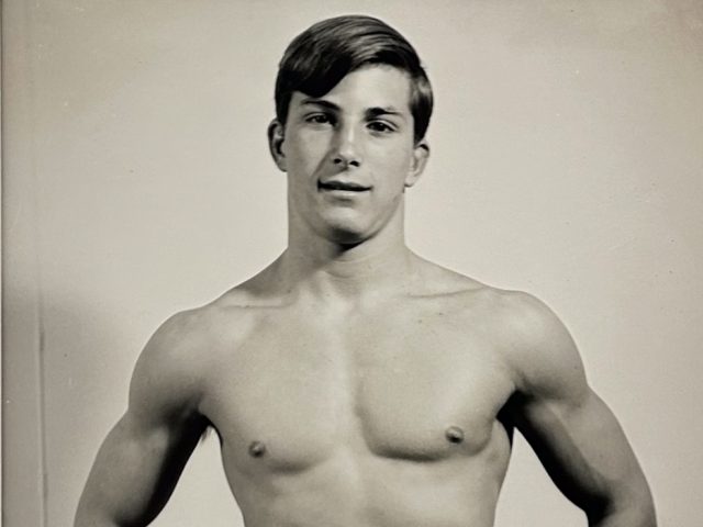 A black and white photograph of a shirtless man with his hands on his hips.