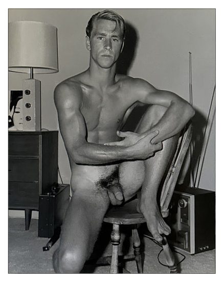 A black and white photograph of a nude man sitting in a chair.
