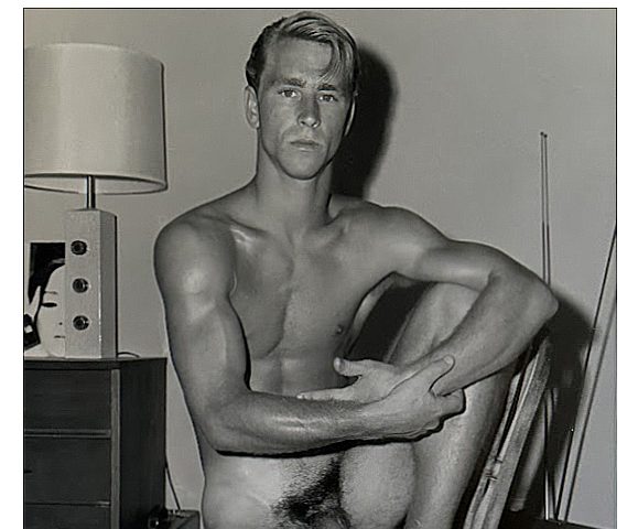A black and white photograph of a nude man sitting in a chair.