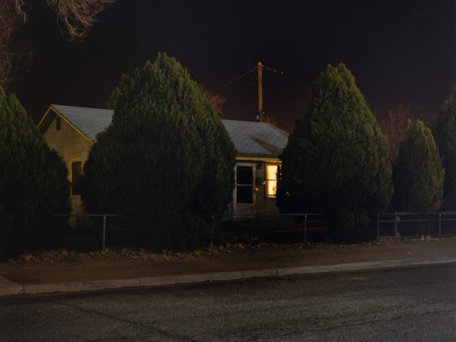 A photograph of a house at night with a single window lit up.