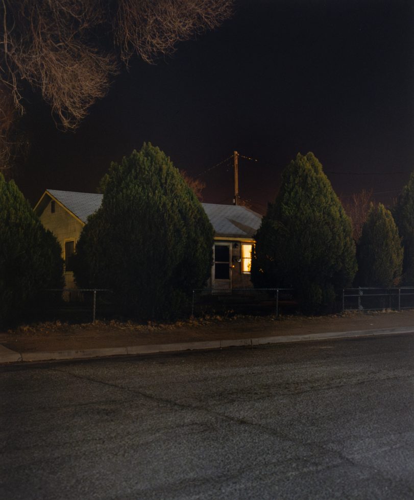A photograph of a house at night with a single window lit up.
