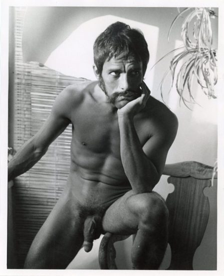 A black and white photograph of a nude man with his elbow resting in his knee.