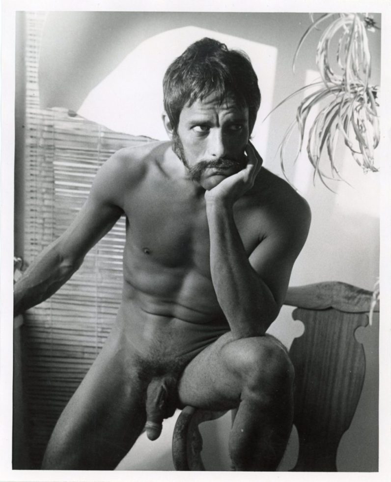 A black and white photograph of a nude man with his elbow resting in his knee.
