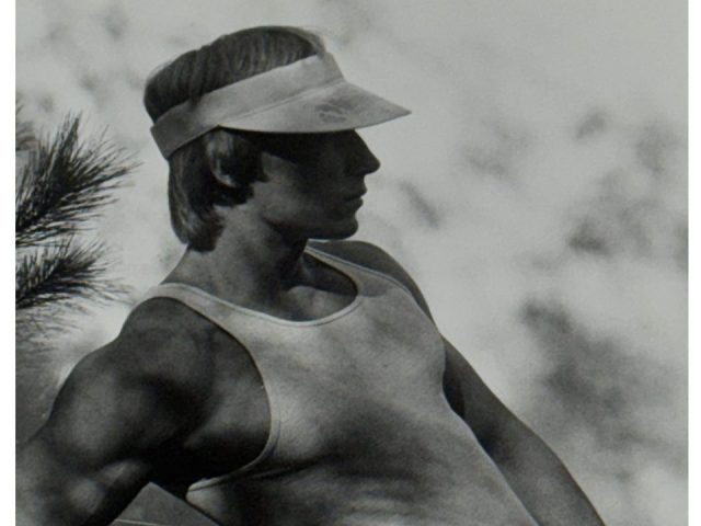 A black and white photograph of a man in gym clothes and a visor.