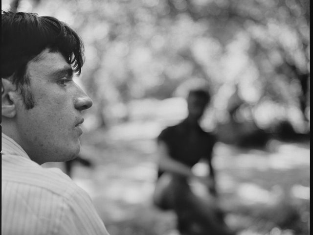 A black and white photograph of a young man sitting in a park.