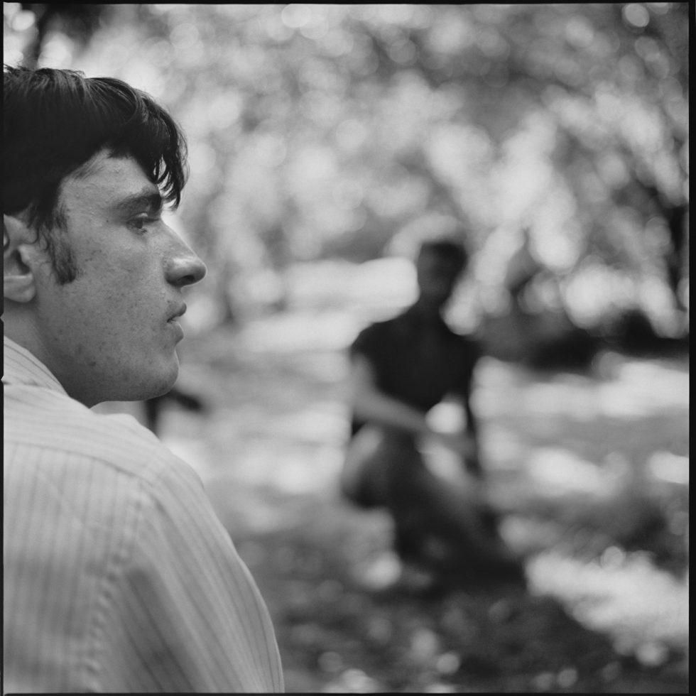 A black and white photograph of a young man sitting in a park.