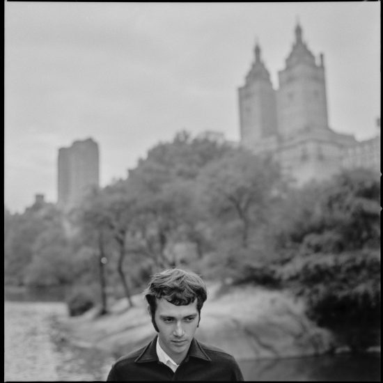 A black and white photograph of a young man standing in central park.