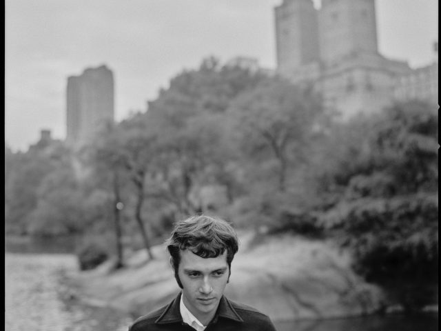 A black and white photograph of a young man standing in central park.