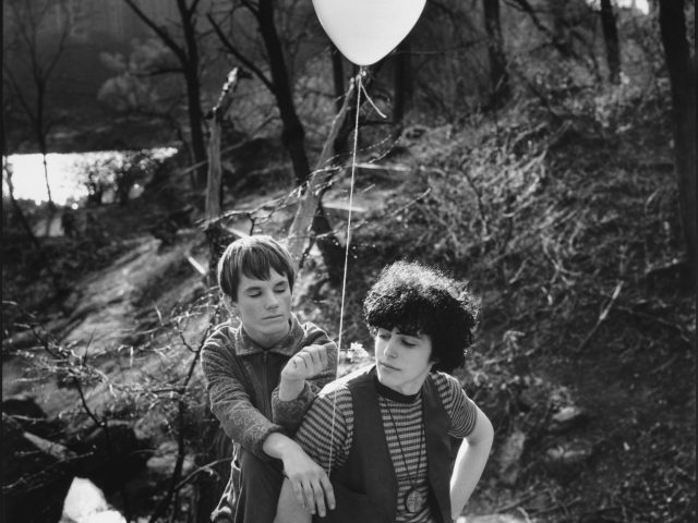 A black and white photograph of two young people in a park holding a balloon.