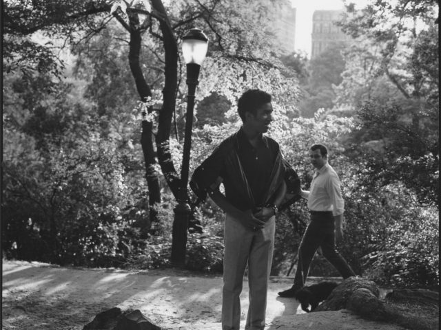 A black and white photograph of a man standing in a park.