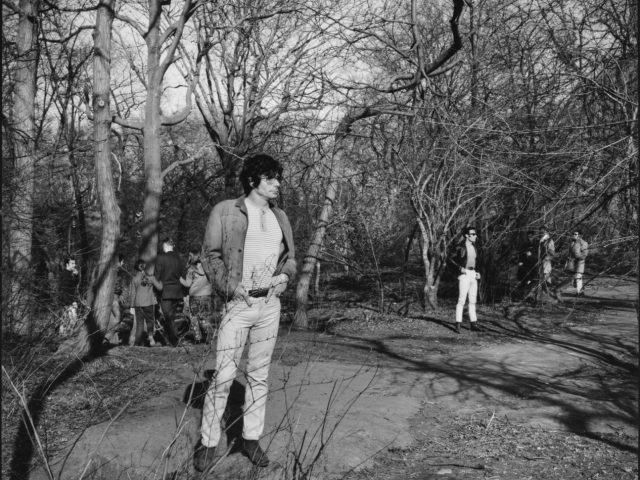 A black and white photograph of a young man in a city park.