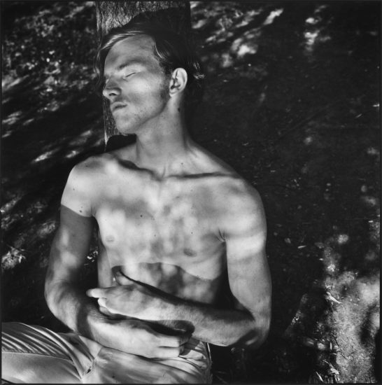 A black and white photograph of a shirtless man in a park.