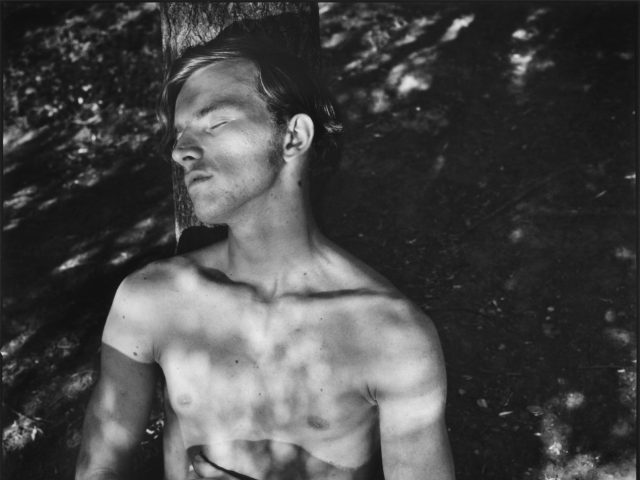 A black and white photograph of a shirtless man in a park.