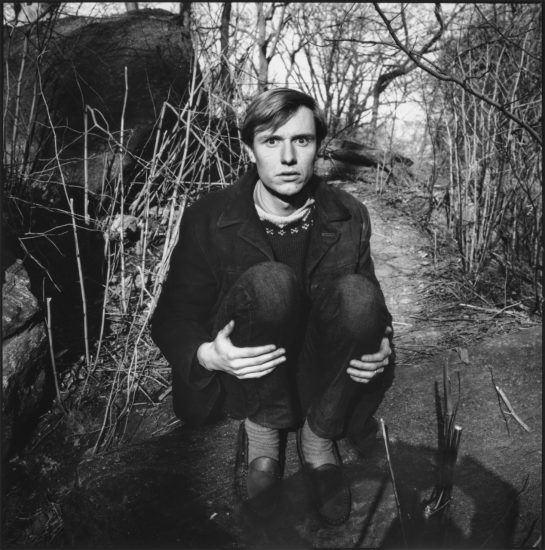 A black and white photograph of a young man crouching in a park.