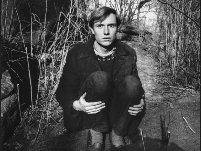 A black and white photograph of a young man crouching in a park.