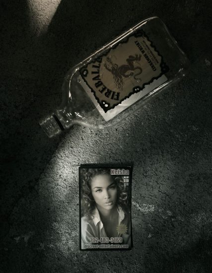 A photograph of an escort card, next to a bottle of Fireball on a sidewalk.