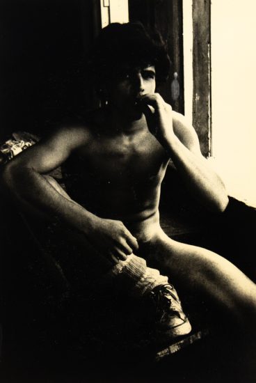 A black and white photograph of a nude young man smoking.
