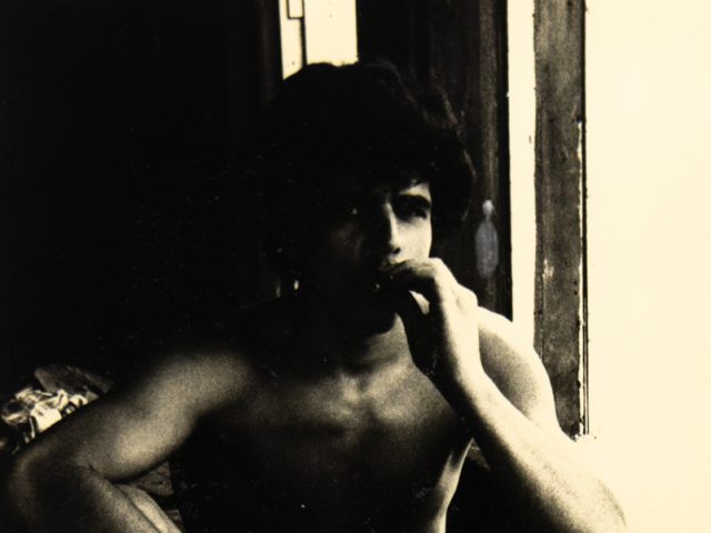 A black and white photograph of a nude young man smoking.