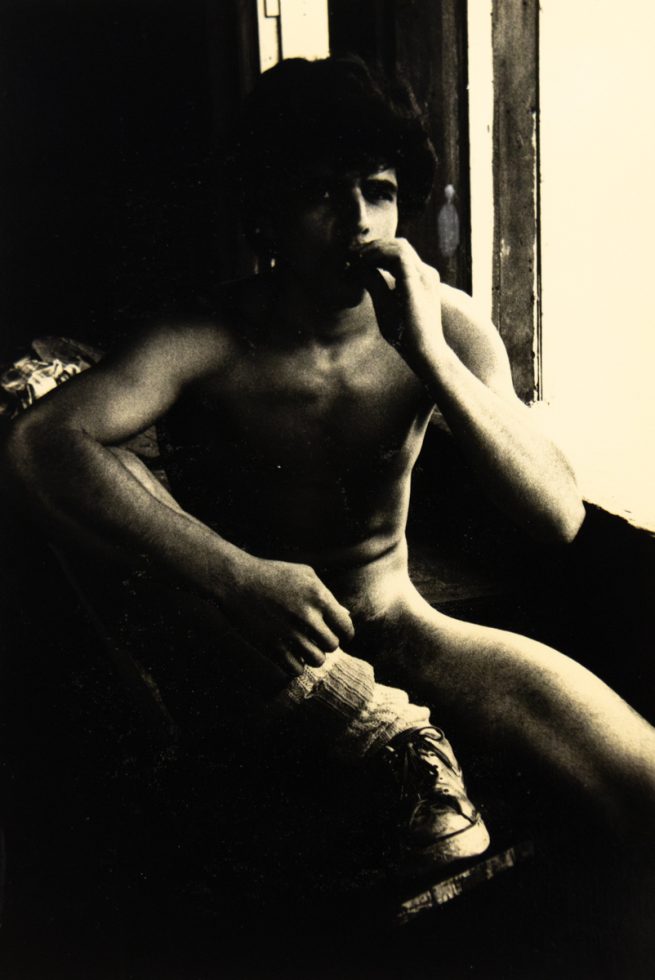 A black and white photograph of a nude young man smoking.