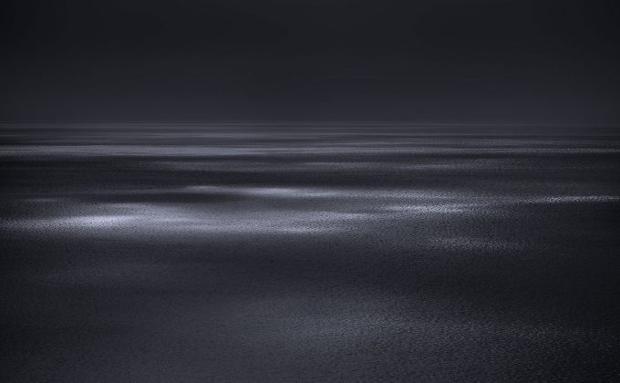 A photograph of a body of water with reflected light on the surface and a horizon line.