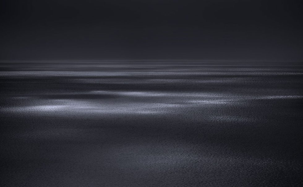 A photograph of a body of water with reflected light on the surface and a horizon line.