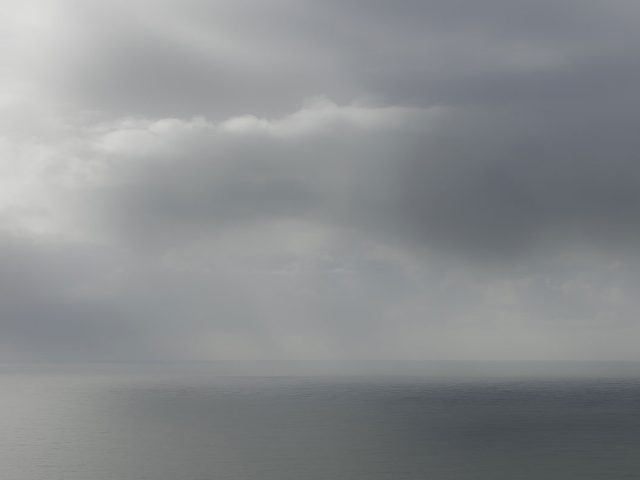 A photograph of a body of water with reflected light on the surface and a horizon line.