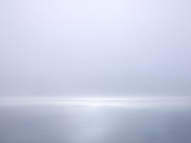 A photograph of a body of water with reflected light on the surface and a horizon line.