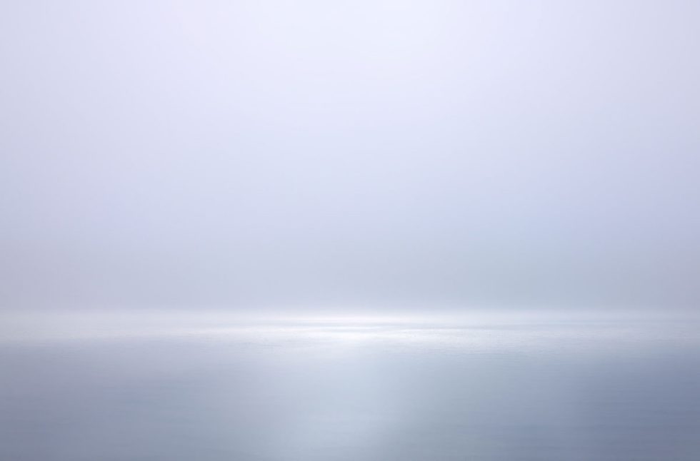 A photograph of a body of water with reflected light on the surface and a horizon line.